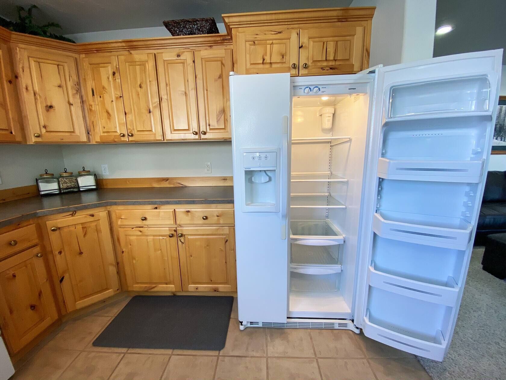 Una cocina con armarios de madera, un refrigerador blanco y un tapete negro en el suelo.