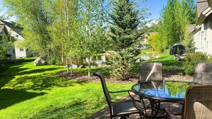 Eine Terrasse mit rundem Tisch und Stühlen, umgeben von einer Rasenfläche und Bäumen.
