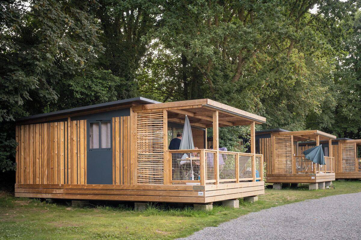 Varias cabañas de madera con porche cubierto y mesa con sillas.