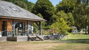 A wooden building with a sloped roof, a covered porch, and a bicycle parking area. - Huttopia Baie du Mont Saint Michel (Baguer-Pican)