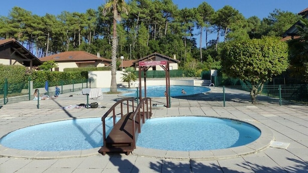 A swimming pool area with a wooden deck, a lifeguard stand, and a small pavilion. - CAPBRETON – Residence LE BOSQUET AUX ECUREUILS. Villa with shared swimming pool. (CAPBRETON)