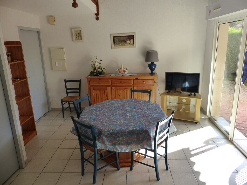 Ein Essbereich mit einem runden Tisch, Stühlen, einer Holzkommode, einem Fernseher und einem Fenster mit Blick auf Grünflächen.