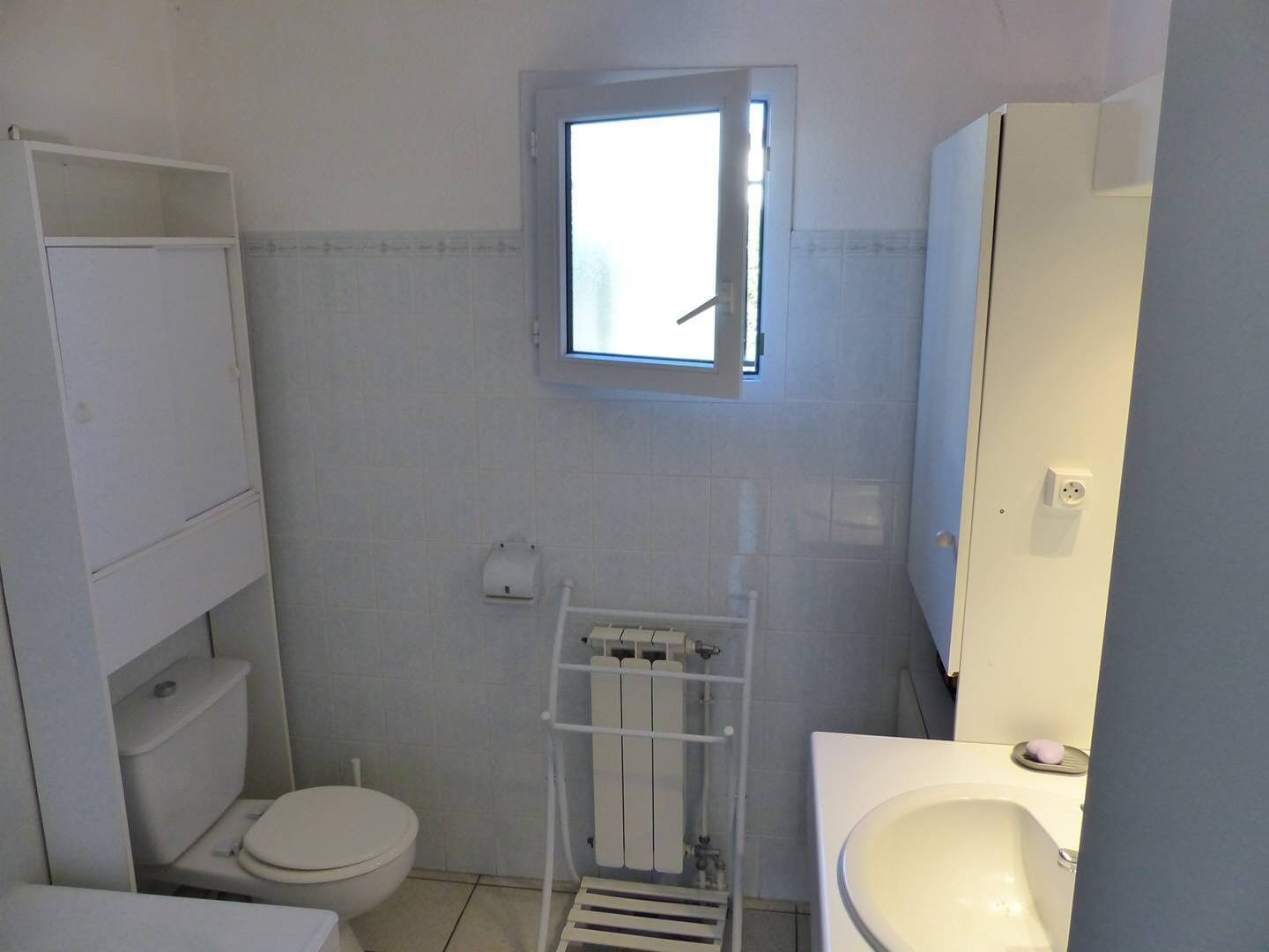 A compact bathroom with a toilet, sink, and a window above the toilet.