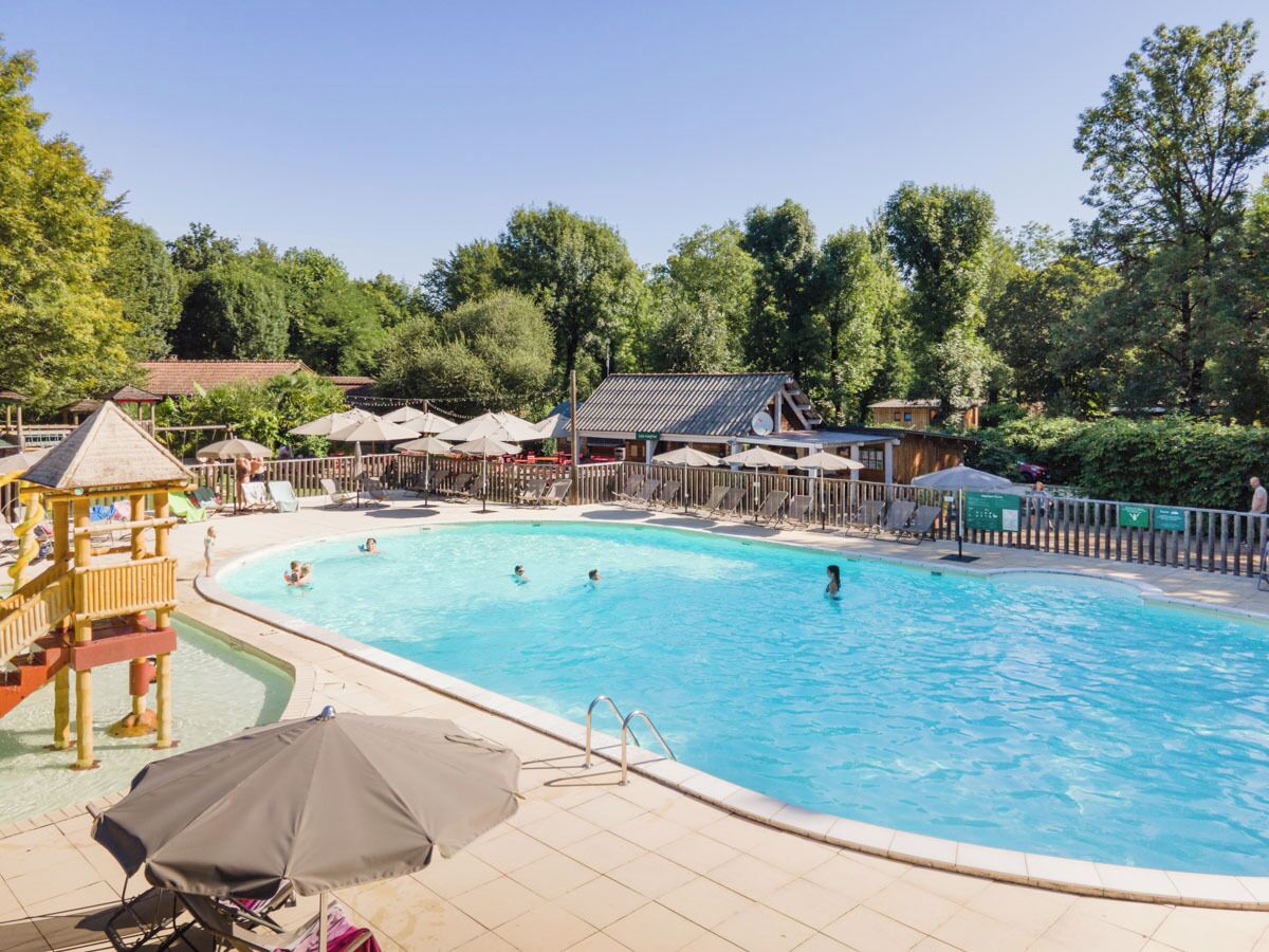 Una amplia piscina exterior con varias pistas, rodeada de sillones y sombrillas, y cubierta por una estructura de madera.