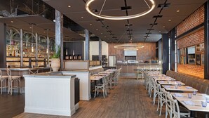 A spacious restaurant with a long counter, multiple tables, and a brick wall. - HOTEL CERRO, Autograph Collection (San Luis Obispo)