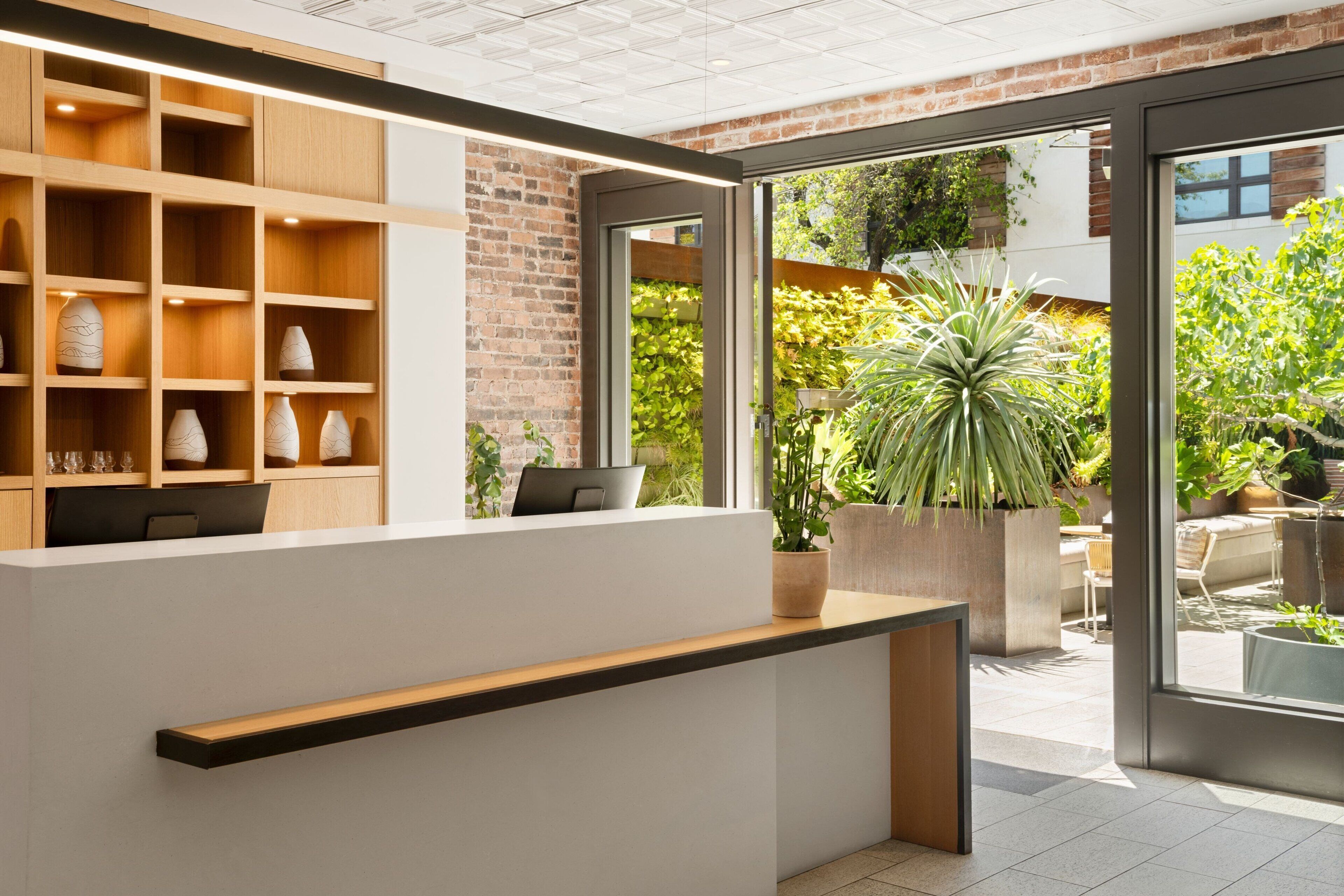A reception area with a wooden shelving unit displaying vases, a reception desk, and a view of an outdoor garden with potted plants.