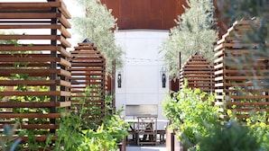 A wooden pergola structure with a table and chairs underneath, surrounded by greenery. - HOTEL CERRO, Autograph Collection (San Luis Obispo)