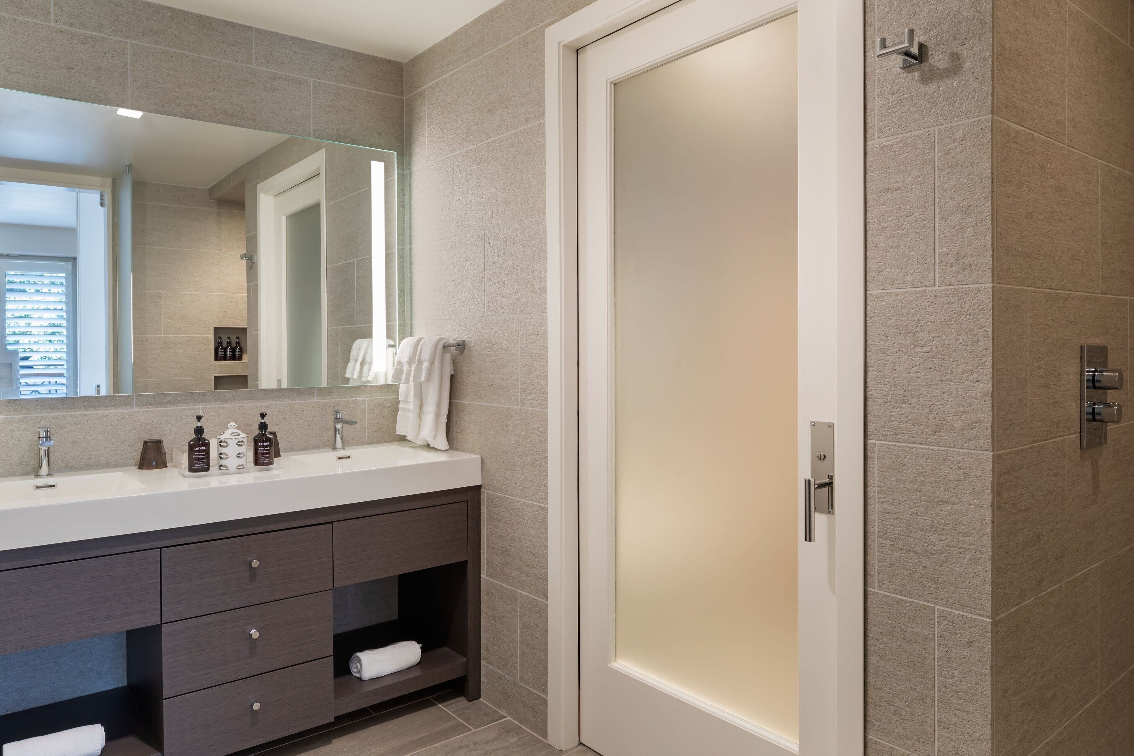 A modern bathroom with a large mirror, a white sink, dark wooden vanity, and a glass shower enclosure.