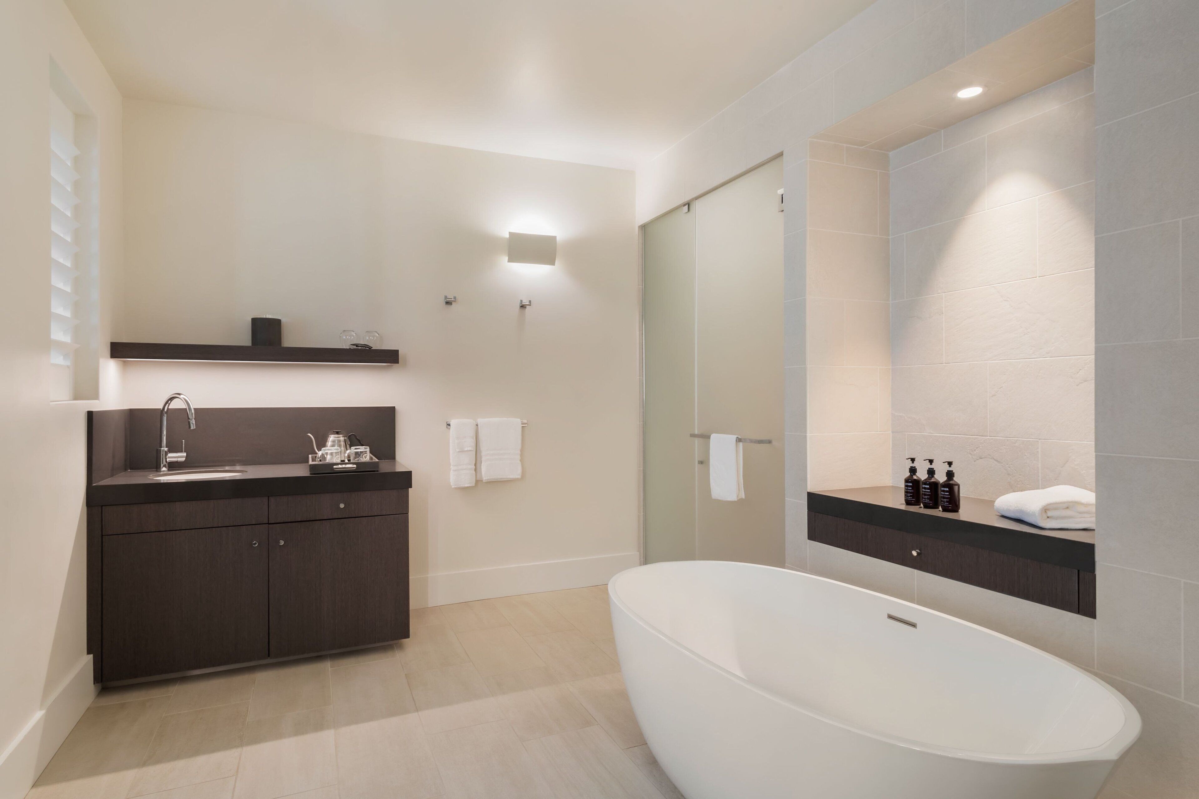 Une salle de bain moderne avec une baignoire sur pieds, un meuble-lavabo en bois foncé, une cabine de douche en verre et un miroir fixé au mur.