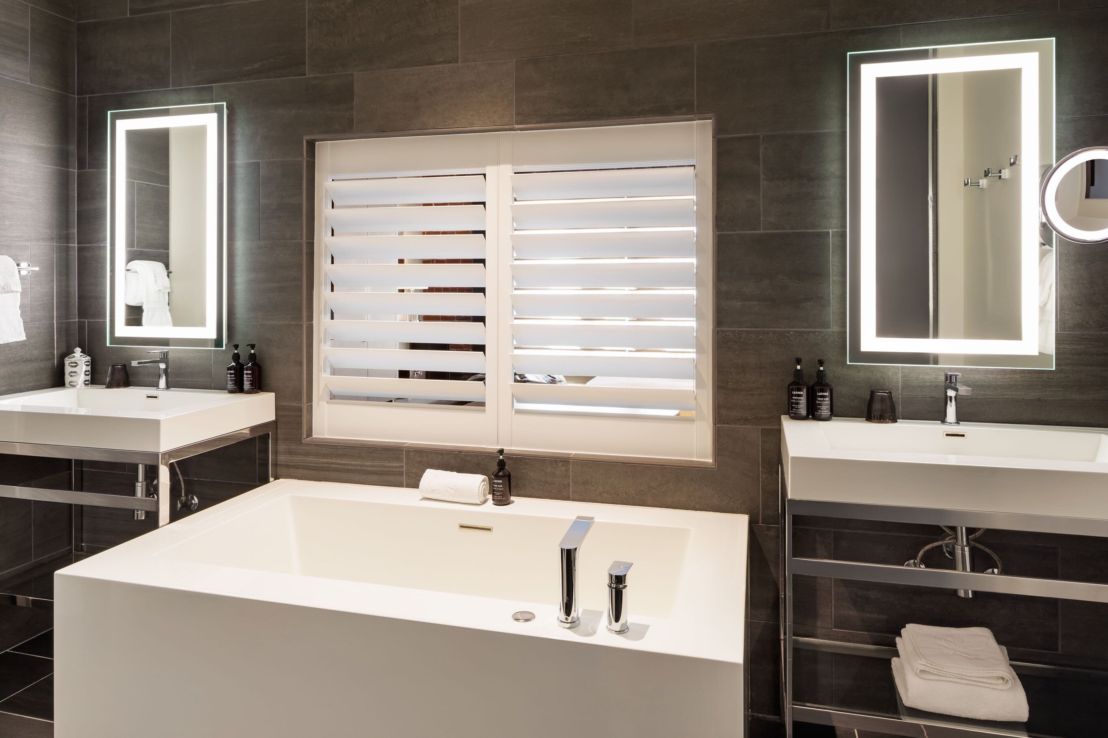 A modern bathroom with two sinks, a large bathtub, and overhead mirrors with lights.