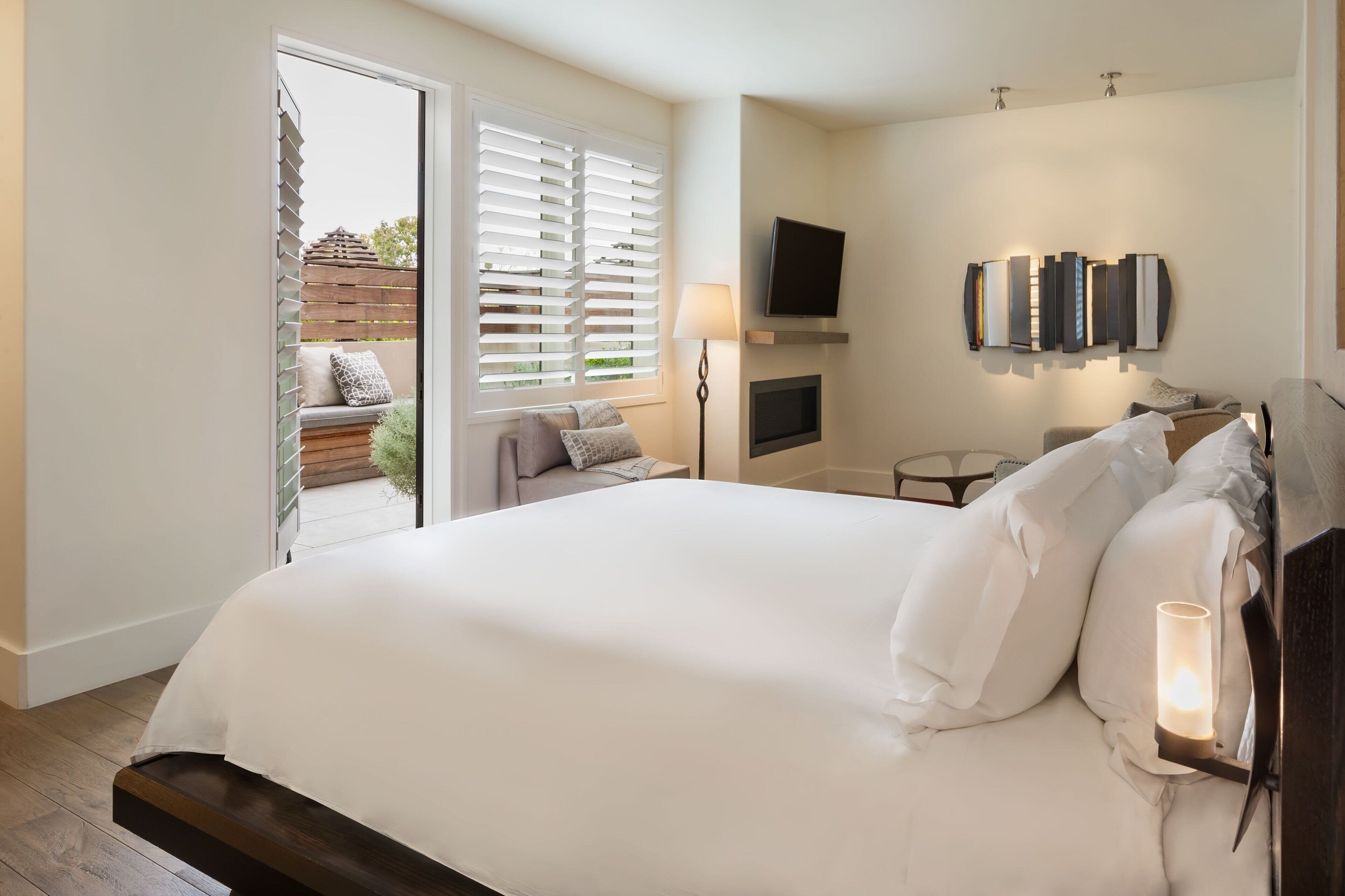Quarto com uma cama grande, televisão na parede e porta de correr para área externa.
