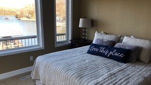Un dormitorio con una cama grande, una ventana con vistas a un lago y una mesita de noche con una lámpara.