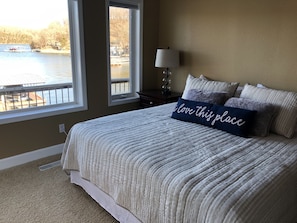 Un dormitorio con una cama grande, una ventana con vistas a un lago y una mesita de noche con una lámpara.
