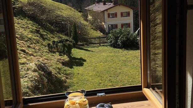 A window view of a house with a mountain backdrop. - Vacation apartment Watzmannblick Maria Gern (Berchtesgaden)
