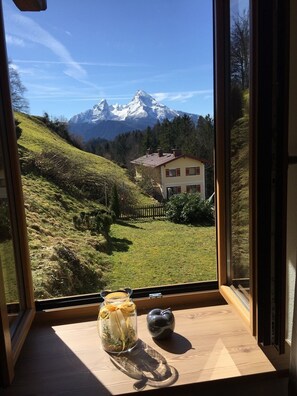 Une vue sur une maison, avec une montagne en arrière-plan, depuis une fenêtre.