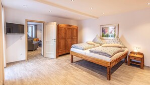 A bedroom with a wooden bed, a nightstand, a wardrobe, and a TV in the adjacent room. - Vacation apartment Watzmannblick Maria Gern (Berchtesgaden)