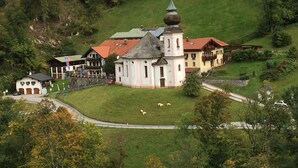 A church with a bell tower and a small bell, surrounded by a grassy area with sheep. - Vacation apartment Watzmannblick Maria Gern (Berchtesgaden)