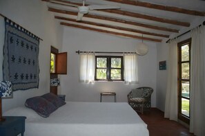 A bedroom with a large bed, a chair, a small table, and a window with curtains.