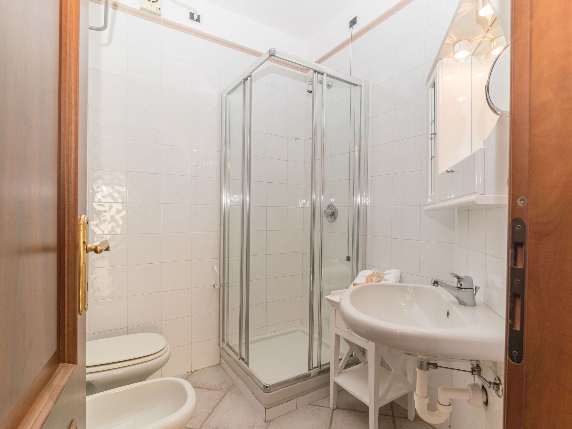 A bathroom with a glass-enclosed shower, a toilet, a bidet, and a sink with a mirror.