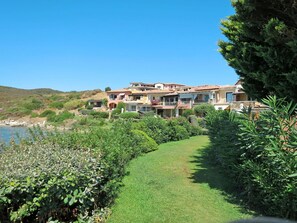 Stunning villas with balconies offer panoramic views of the coastline, surrounded by lush greenery and a well-manicured pathway.