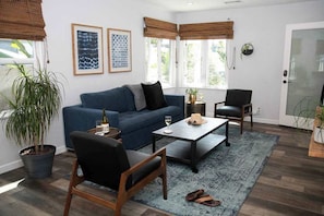 A living room with a blue sofa, a coffee table, a chair, a potted plant, and a window with blinds.