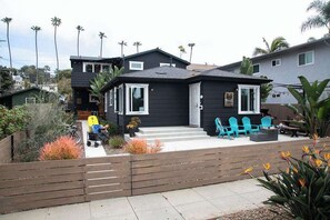 A two-story house with a patio area, outdoor seating, and a wooden fence.
