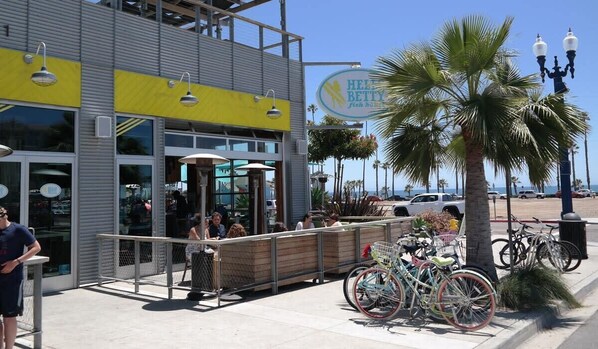 A coastal restaurant with outdoor seating, a palm tree, and bicycles parked outside.