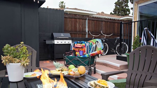 Eine Terrasse mit Grill, einem Esstisch gedeckt mit Speisen, einem Blumentopf und Gartenmöbeln.
