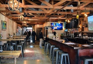 A rustic bar with wooden beams, metal stools, and a variety of bottles and glasses on the shelves. - Kauai-Inspired California Beach Retreat, Unit 1 (Oceanside)