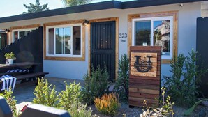 A building with a number '323 One' on the door, a wooden sign with a letter 'U', and a bench outside. - Kauai-Inspired California Beach Retreat, Unit 1 (Oceanside)