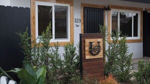 Un edificio moderno con dos ventanas, una puerta de madera con un logotipo y el número '323' en la pared.
