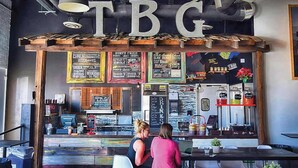 Un restaurante con un letrero grande que dice 'TBG', un menú en una pizarra y una zona de bar.