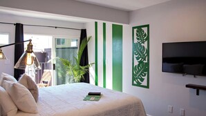 Un dormitorio con cama, televisor, ventana con cortinas, planta y decoración verde en la pared.