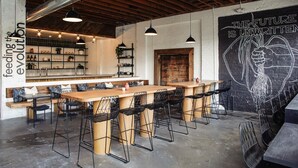 A modern restaurant interior with exposed wooden beams, pendant lighting, bar seating, and a mural on the wall. - Kauai-Inspired California Beach Retreat, Unit 2 (Oceanside)