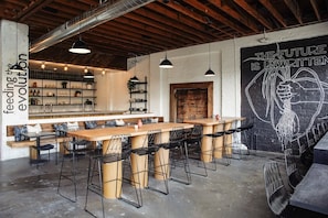 Ein modernes Café mit sichtbaren Holzbalken, schwarzen Metallstühlen und einem Wandgemälde.