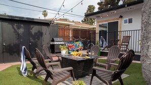 Un espacio exterior para comer con una parrilla, sillas y una mesa lista para una comida.
