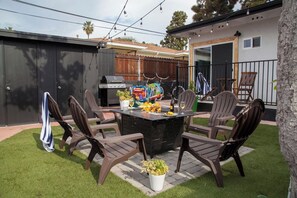 Un espace extérieur aménagé pour les repas, avec un barbecue, des chaises et une table dressée pour un repas.