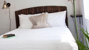 Een net opgemaakt bed met witte lakens, een bruin hoofdbord en twee bedlampjes.