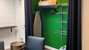 A room with a chair, a metal rack with towels, a green wall, and a window with curtains.