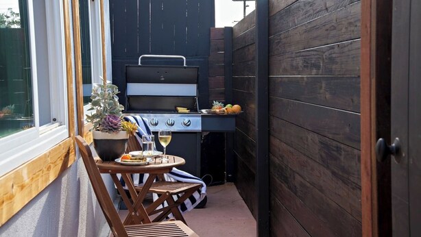 A patio with a grill, a table with a potted plant, and a chair.