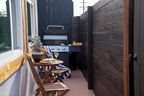 A patio with a grill, a table with a potted plant, and a chair. - Kauai-Inspired California Beach Retreat, Unit 3 (Oceanside)