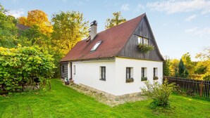 Ett vitt hus med ett mörkt tak, en skorsten och en liten trädgård med ett staket av trä.