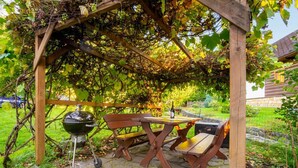 En pergola av trä med ett bord och stolar, en grill och en vinflaska.