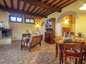 A rustic dining area with a wooden table and chairs, a fireplace, and a kitchen area with a cabinet and archway.