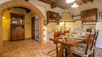Una cucina rustica con travi a vista in legno, un arco in mattoni e un'area pranzo con tavolo e sedie in legno.