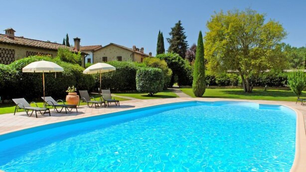 Ein Swimmingpool mit Liegestühlen und Sonnenschirmen, umgeben von gepflegten Hecken und Bäumen.