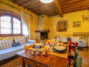 A cozy dining area with a wooden table set for a meal, a sofa with cushions, and a fireplace in the background.