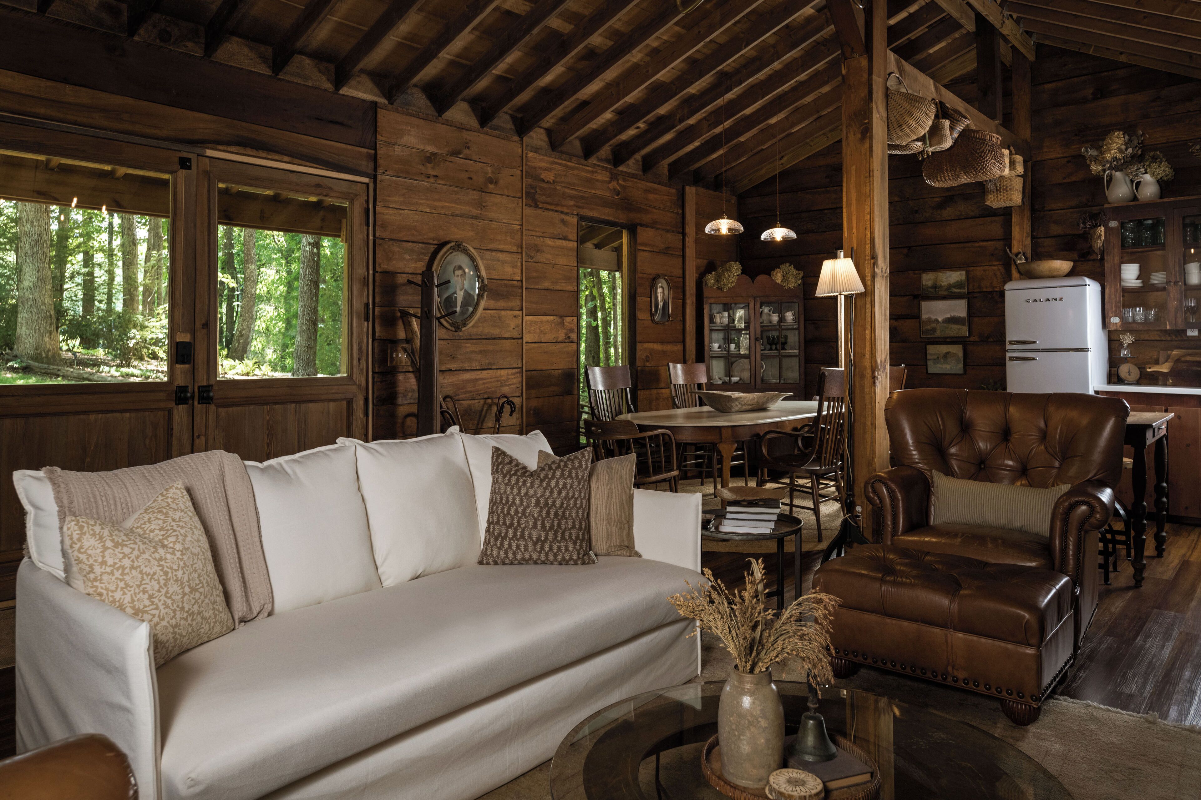 Een houten chalet inrichting met een bank, fauteuil, eettafel en een koelkast.
