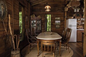 Ein Interieur einer Holzhütte mit Esstisch, Stühlen, einem Kühlschrank und einem Schrank.