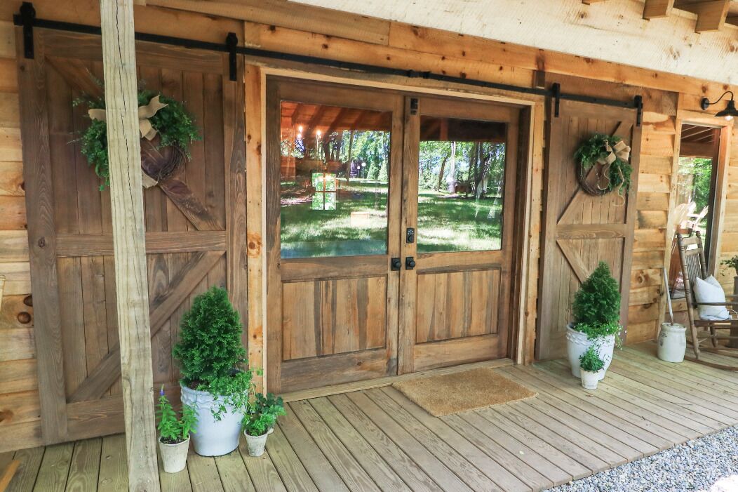 A wooden cabin with a porch, large wooden doors, and potted plants.